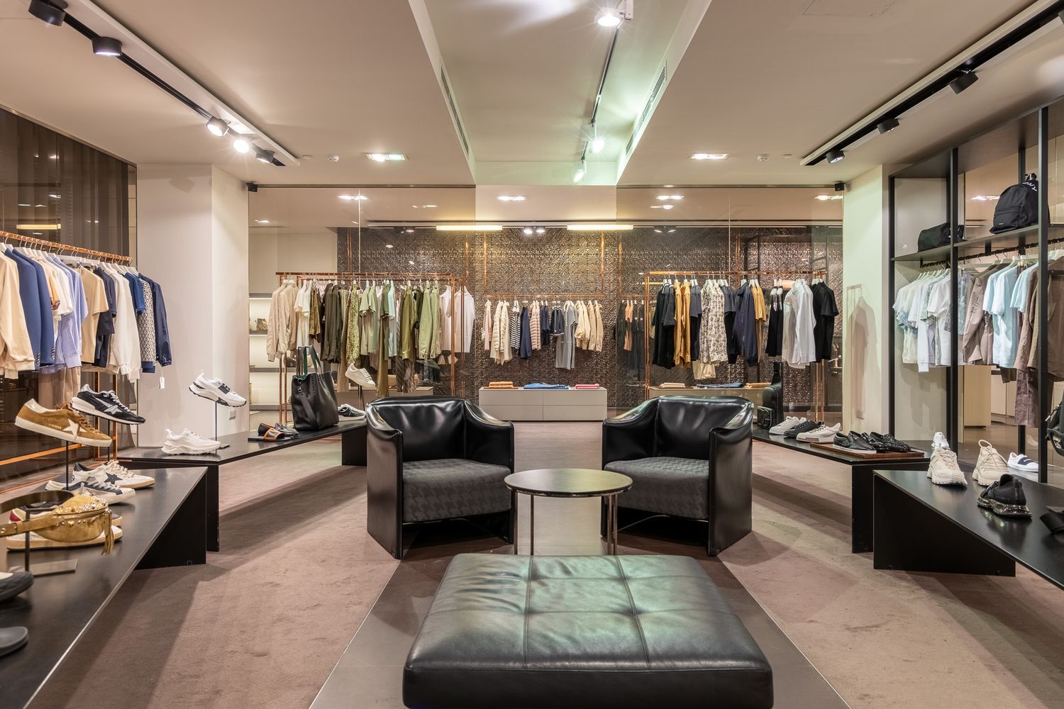 Luxury menswear boutique interior with black leather chairs, clothing racks, and designer shoes on display.