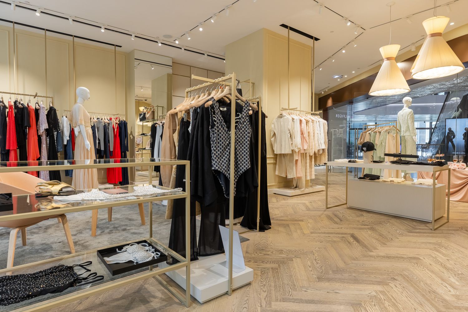 Modern women's fashion boutique with light wood floors, gold clothing racks, and colorful garments on display.