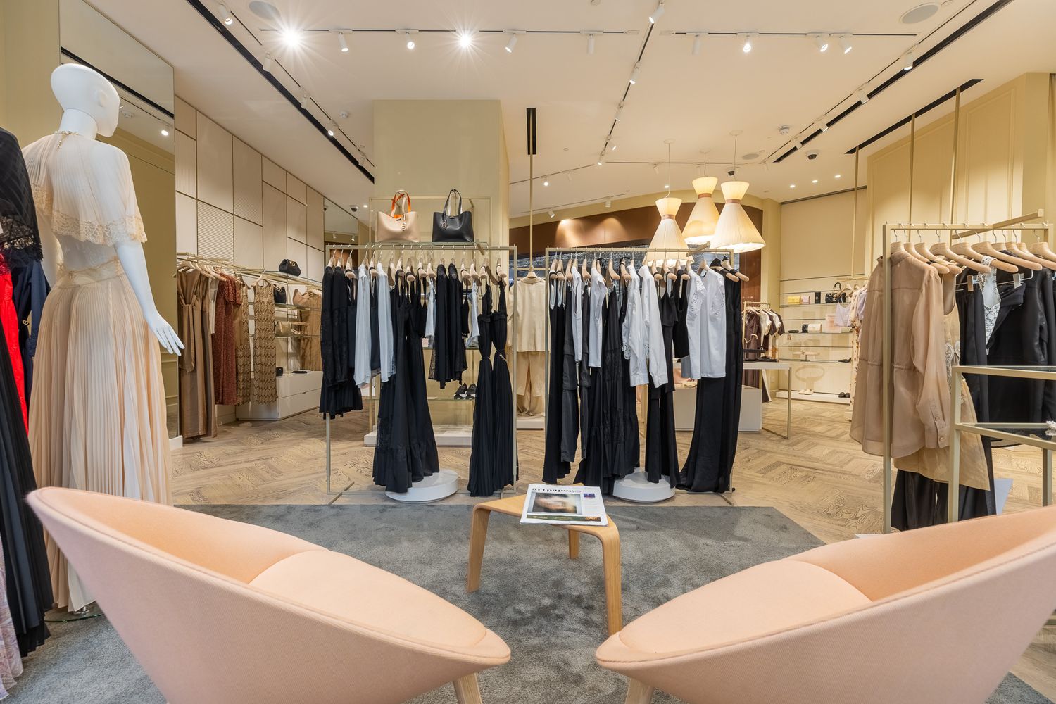 Elegant women's clothing store interior with neutral tones, pink chairs, and garments on display racks.