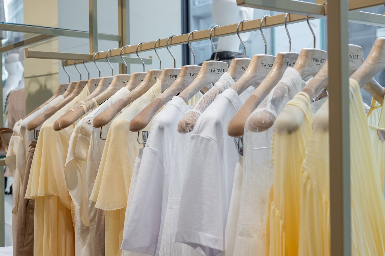 Close-up of neutral-toned clothing including white shirts and yellow garments hanging on a retail rack.
