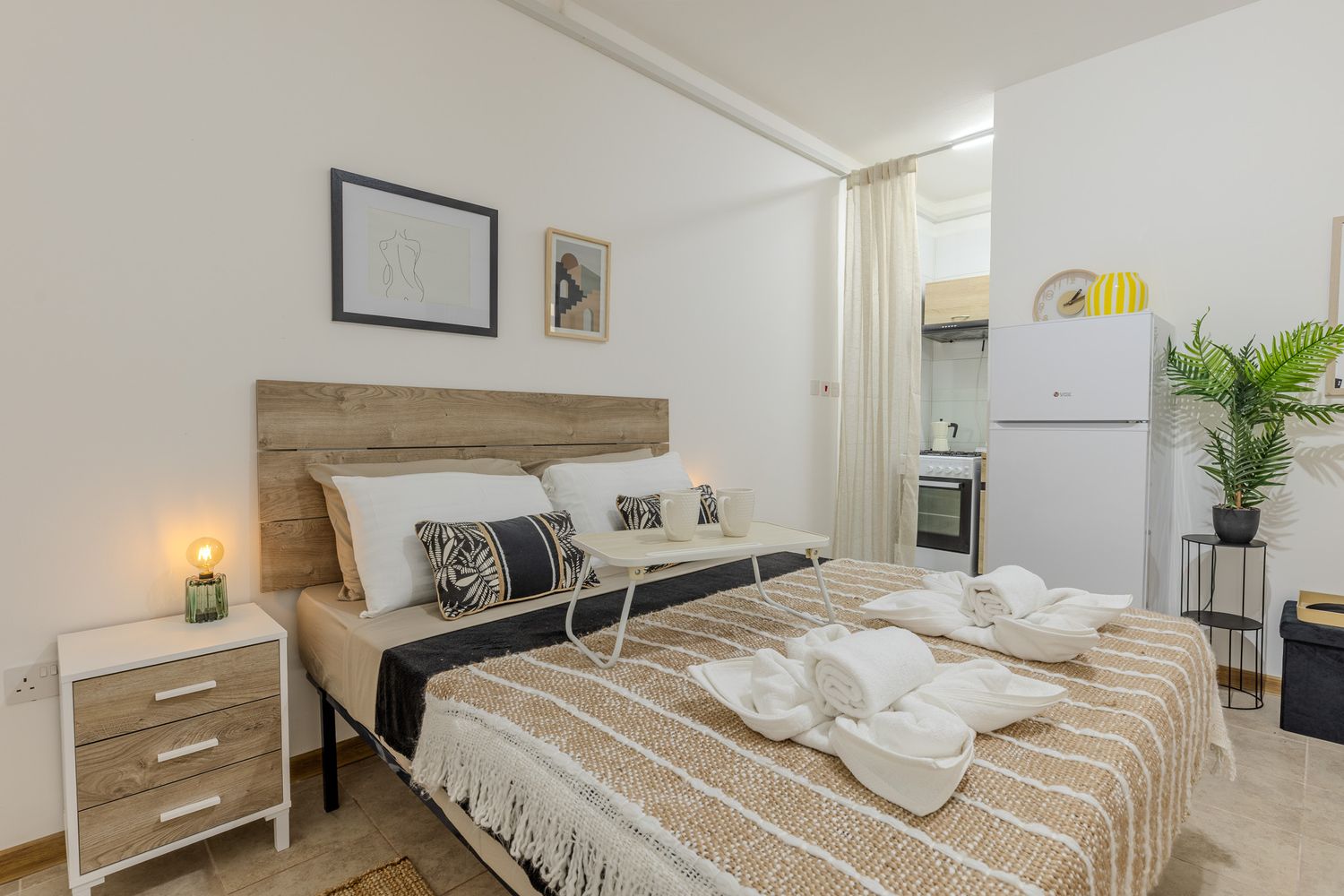 Bright studio apartment featuring a double bed with bohemian decor, wooden headboard, and open kitchen.