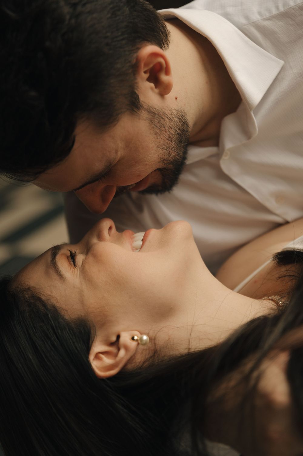 A couple sharing an intimate moment, nearly kissing, the woman smiling with gold earrings as warm light falls across their faces.