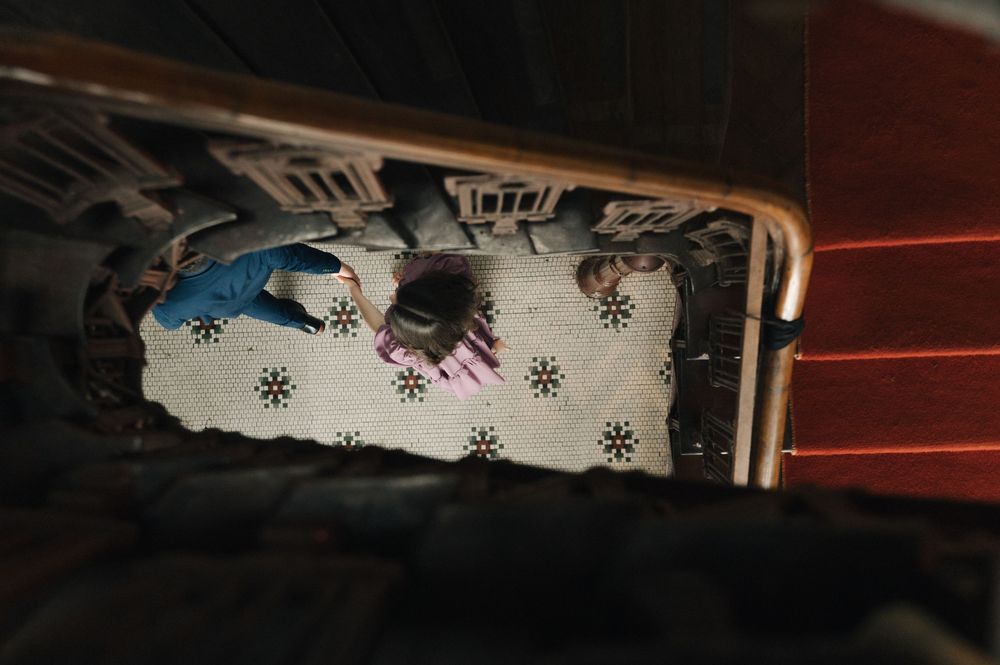 Aerial view of two children lying on a floral patterned rug near wooden staircase railing.