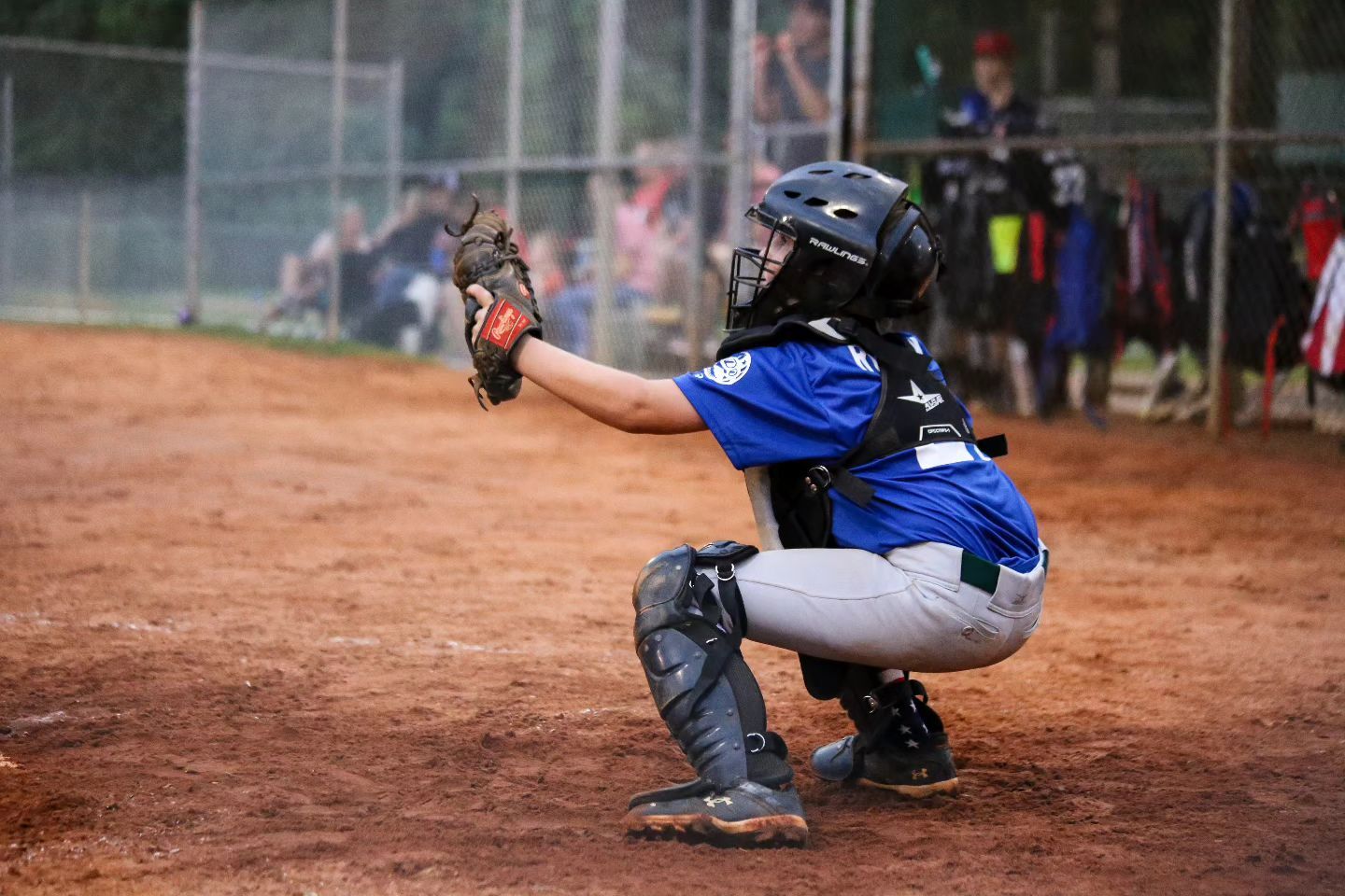 Little le baseball player in catchers stance getting ready to catch a pitch from the pitcher during baseball game.