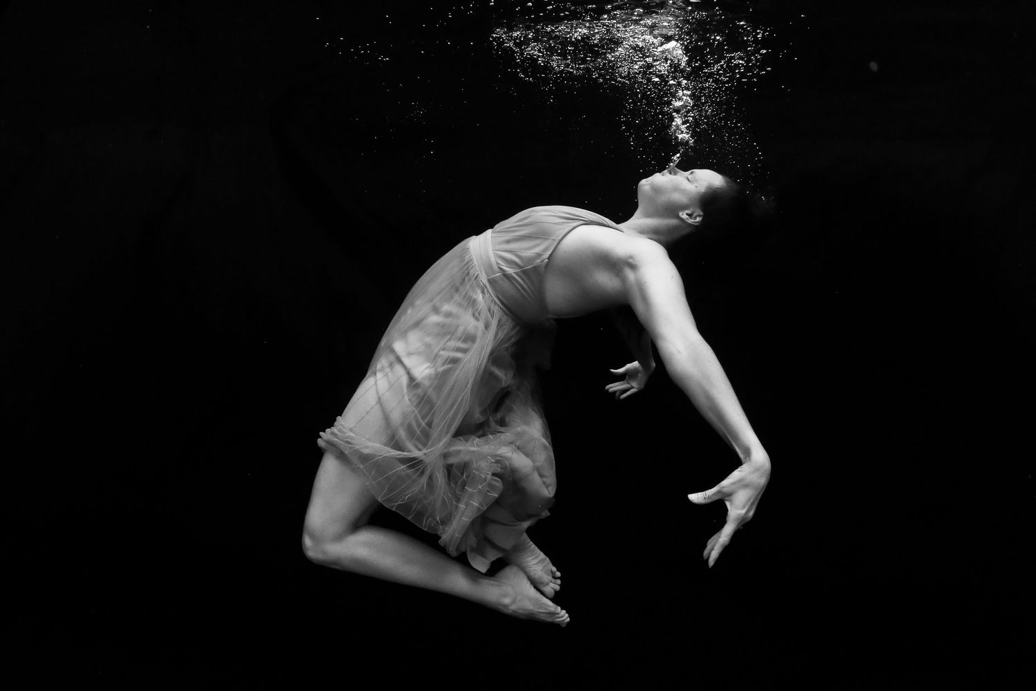 Mom in the frame as underwater dancer blowing bubbles in black and white image.