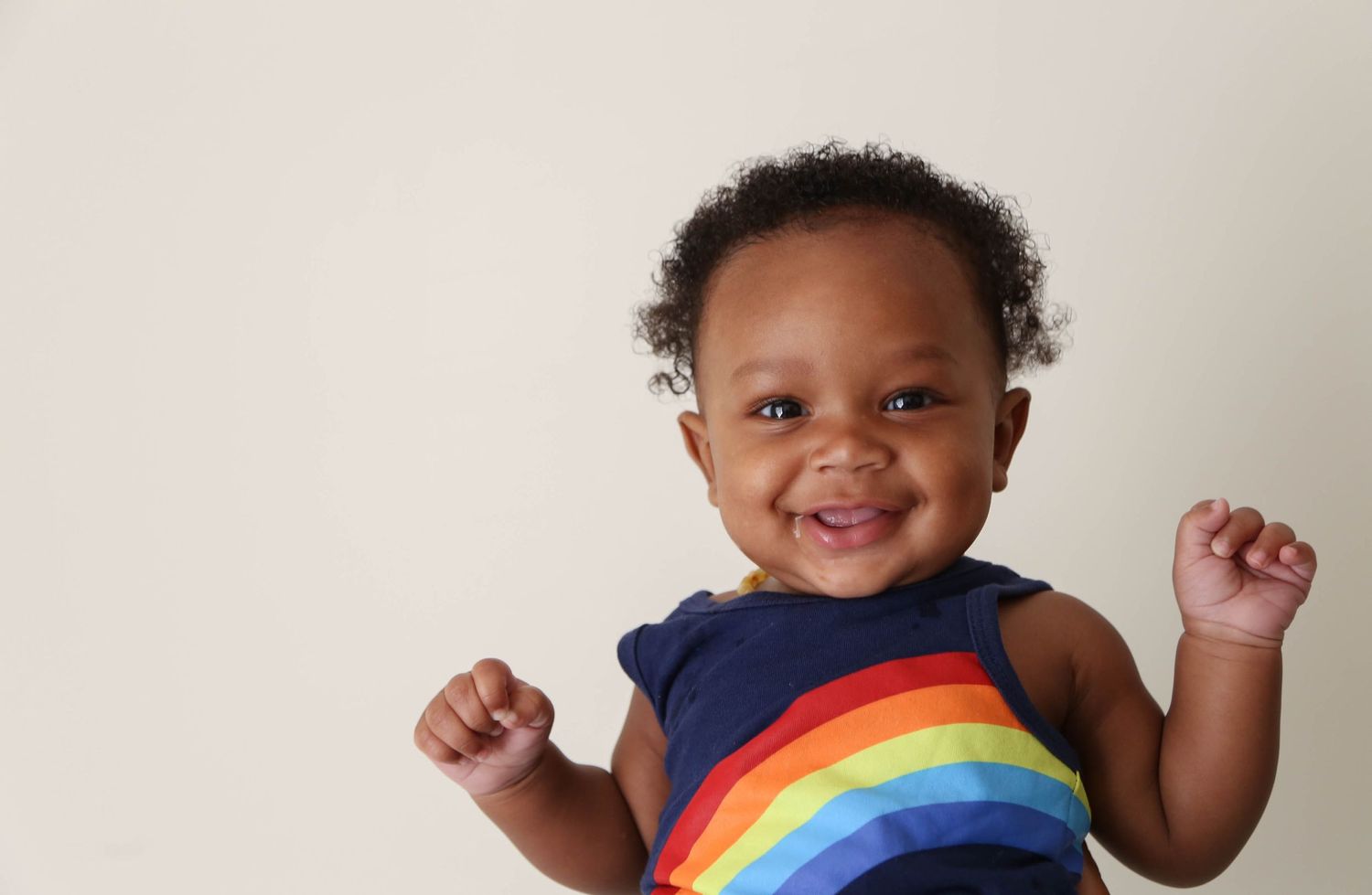 Happy rainbow baby during 6 month milestone picture wearing a rainbow romper.
