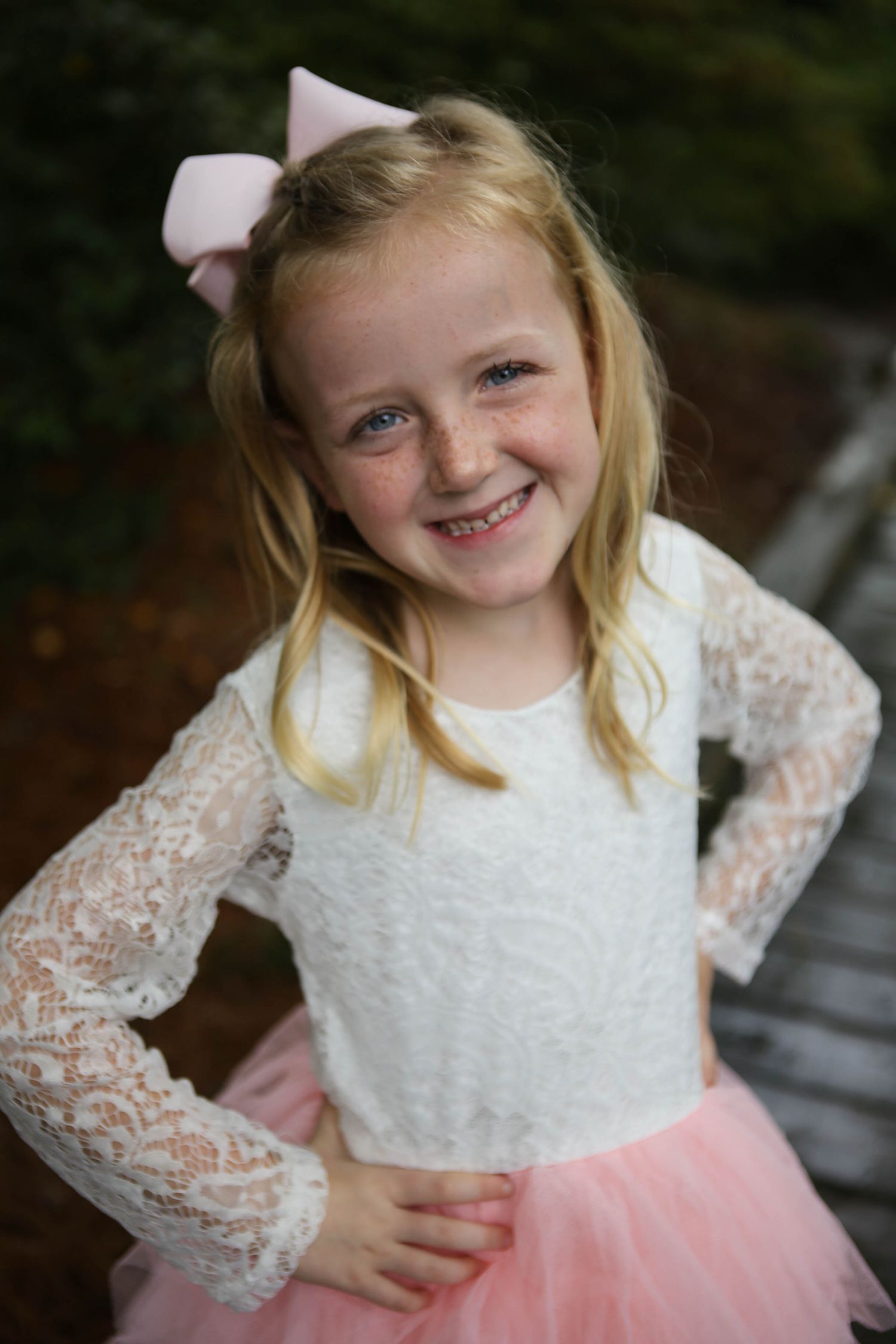 Little girl in white dress, pink tutu and pink bow posing and giving a princess smile.