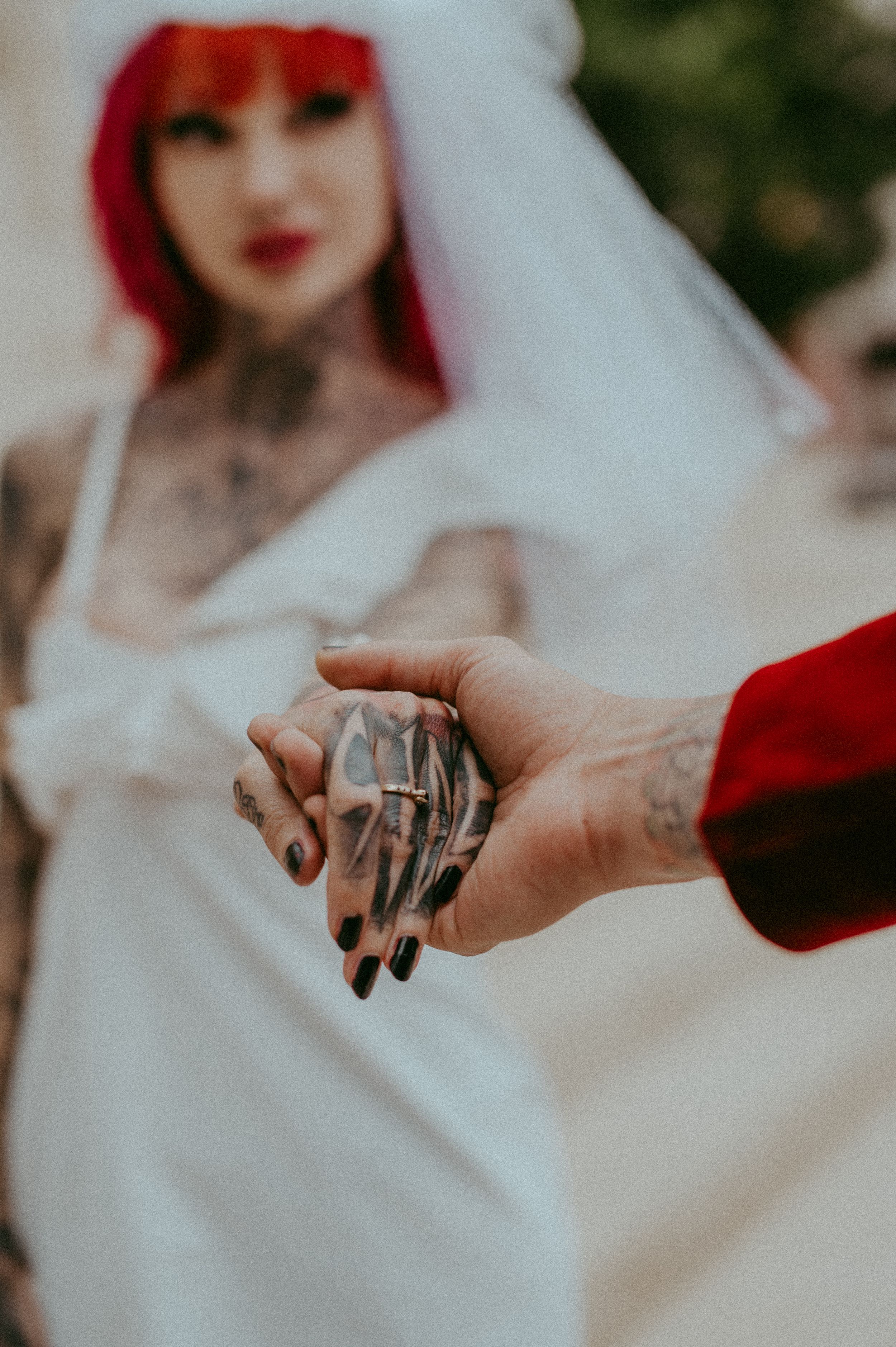 Close-up photo of hands holding a tattooed hand against a blurred white and red background.