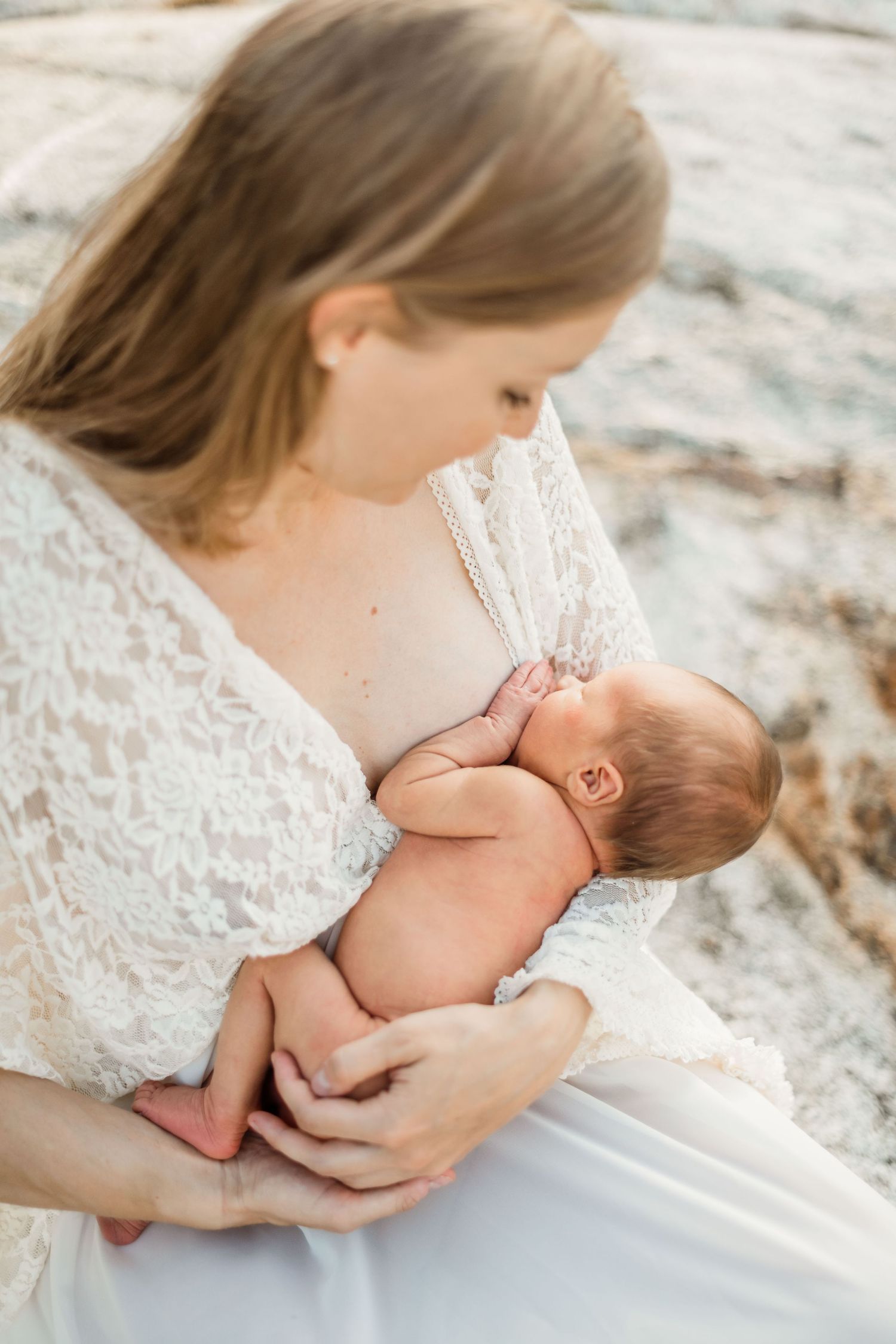 A tender moment between parent and newborn baby in white lace dress against soft natural background.