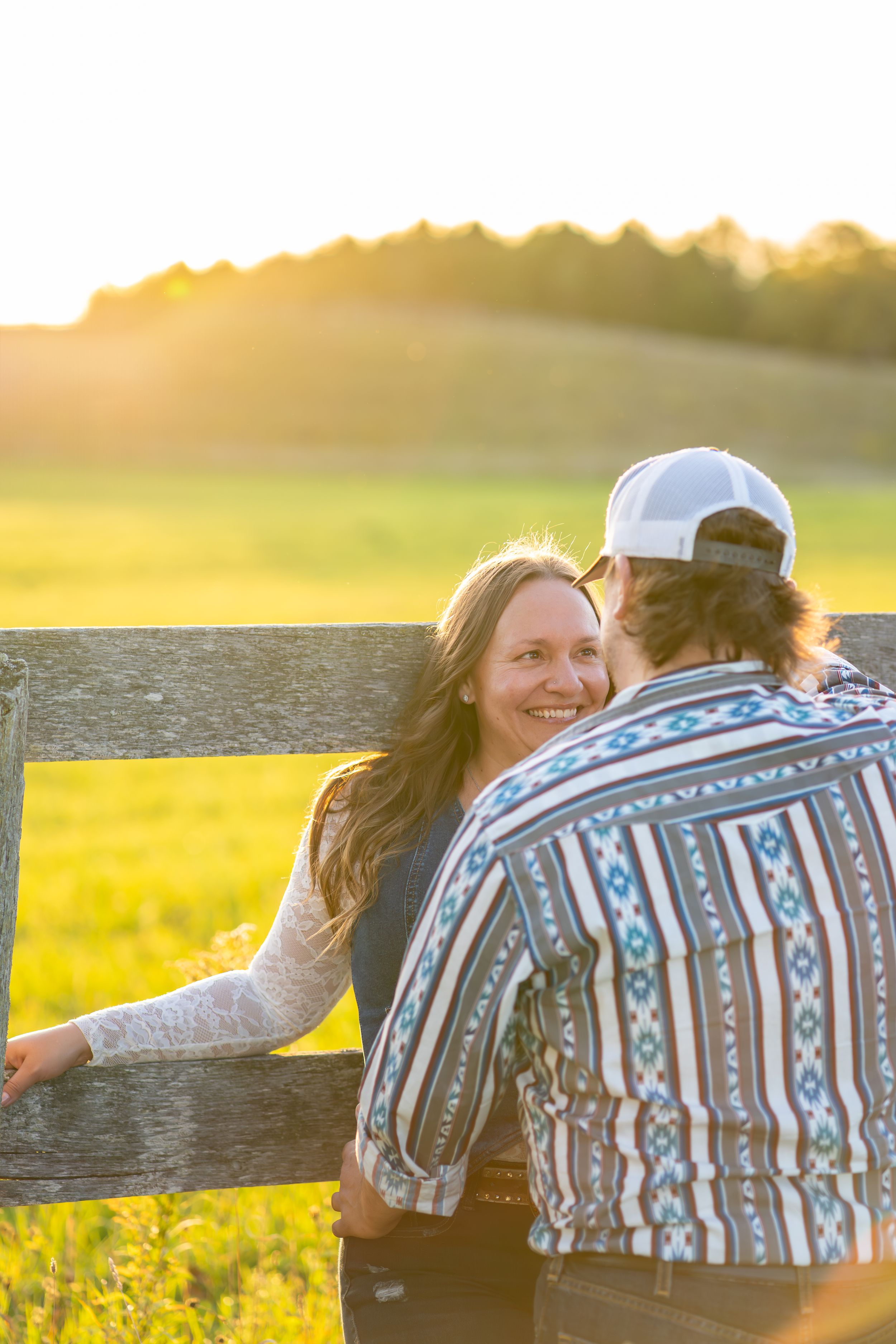 A couple shares a romantic moment at a wooden fence during golden hour sunset in a flowering meadow.