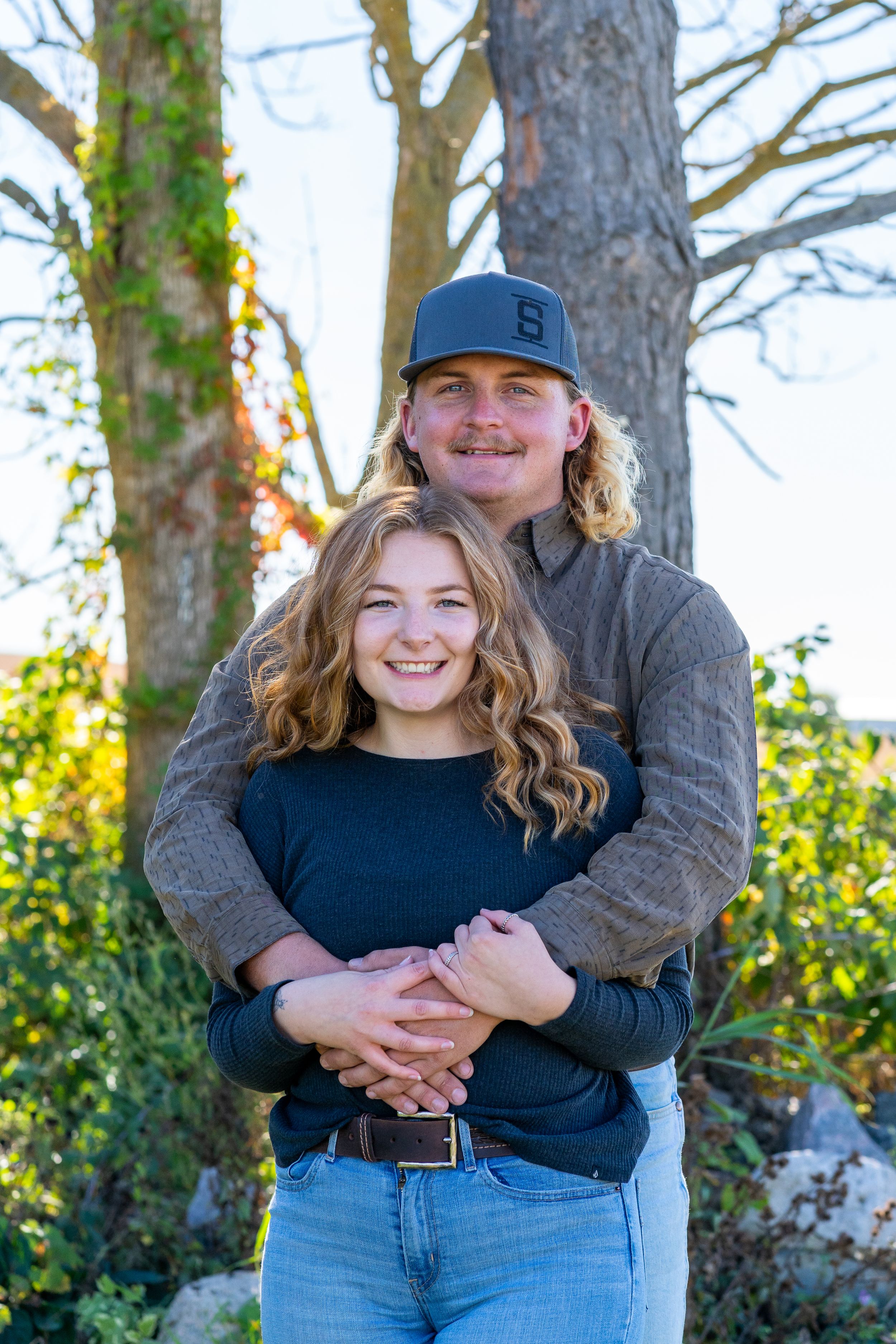 Couple embraces while posing for outdoor portrait among autumn trees.