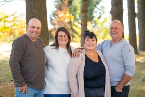 Four adults stand together outdoors during autumn with trees in background.