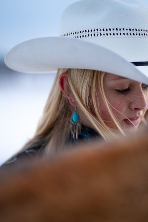 Close-up detail of a white cowboy hat and turquoise earring against a bright background.