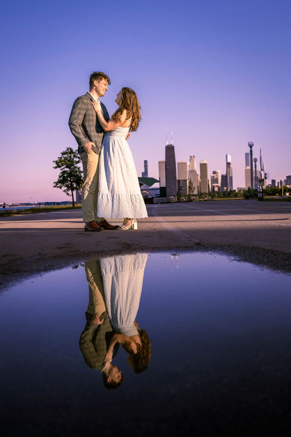 Couple dancing at sunset with Chicago skyline reflected in a puddle behind them.