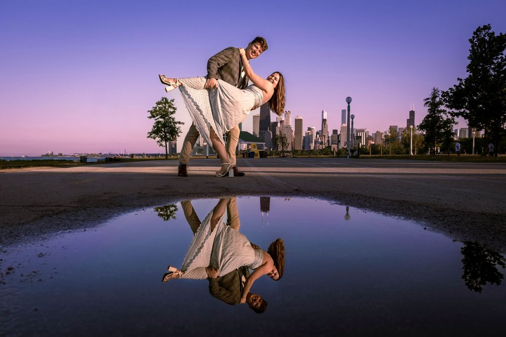 Couple dancing at dusk with Chicago skyline reflected in puddle.