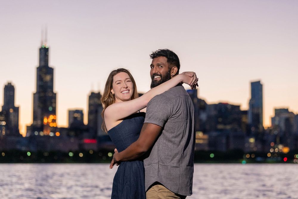 Couple embracing at dusk with Chicago skyline and Willis Tower in background near waterfront.