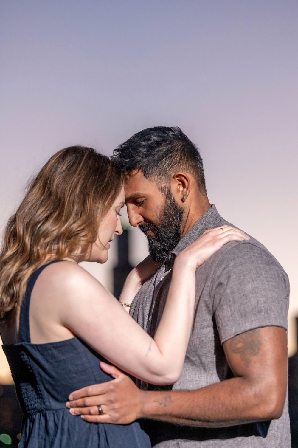 A couple shares an intimate moment at sunset, foreheads touching, as the man embraces the woman in a tender romantic pose.