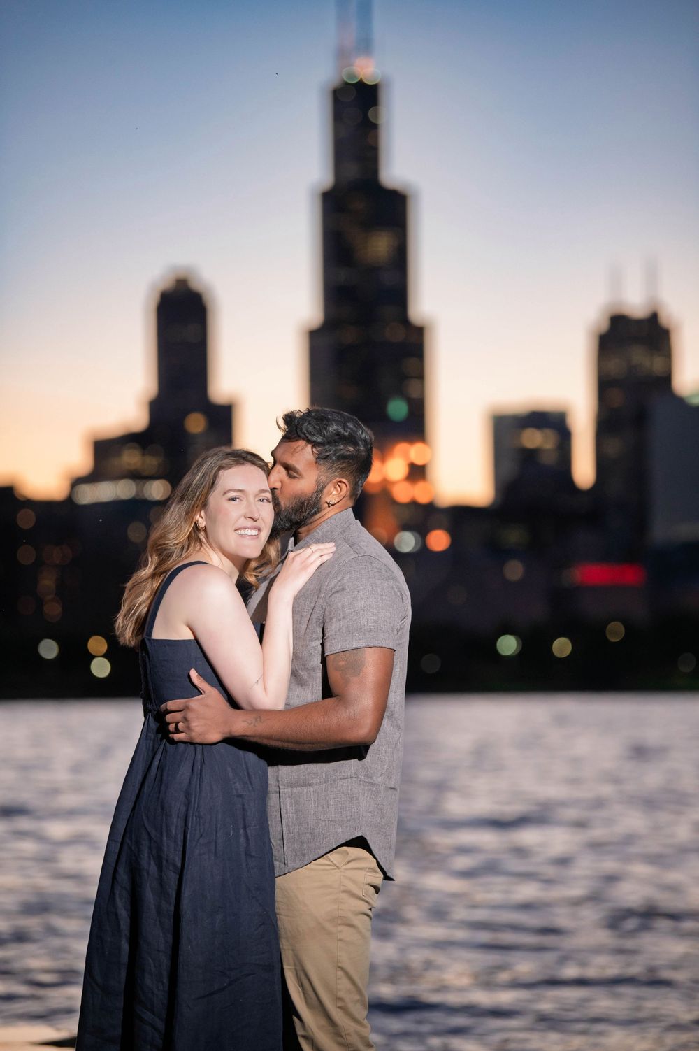 Couple embracing at sunset with Chicago skyline and Willis Tower in the background near the waterfront.