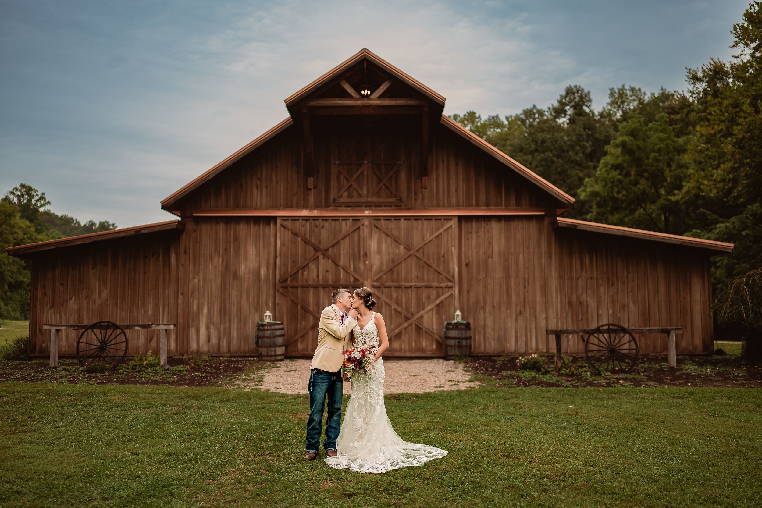 A rustic wooden barn serves as a backdrop for a romantic countryside wedding photoshoot at sunset.