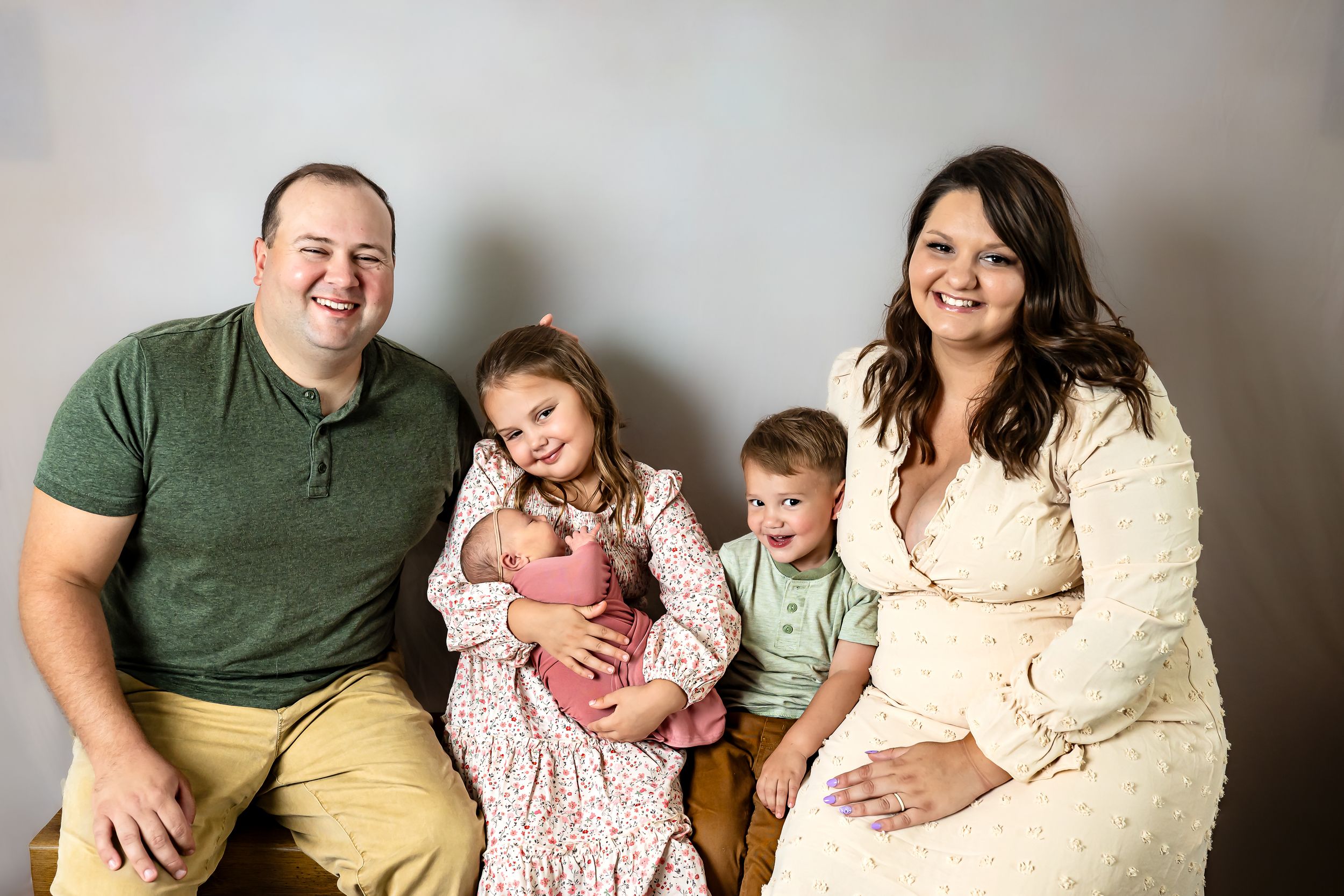 Happy family of five posing together, parents with three young children including a newborn, in a professional studio portrait.
