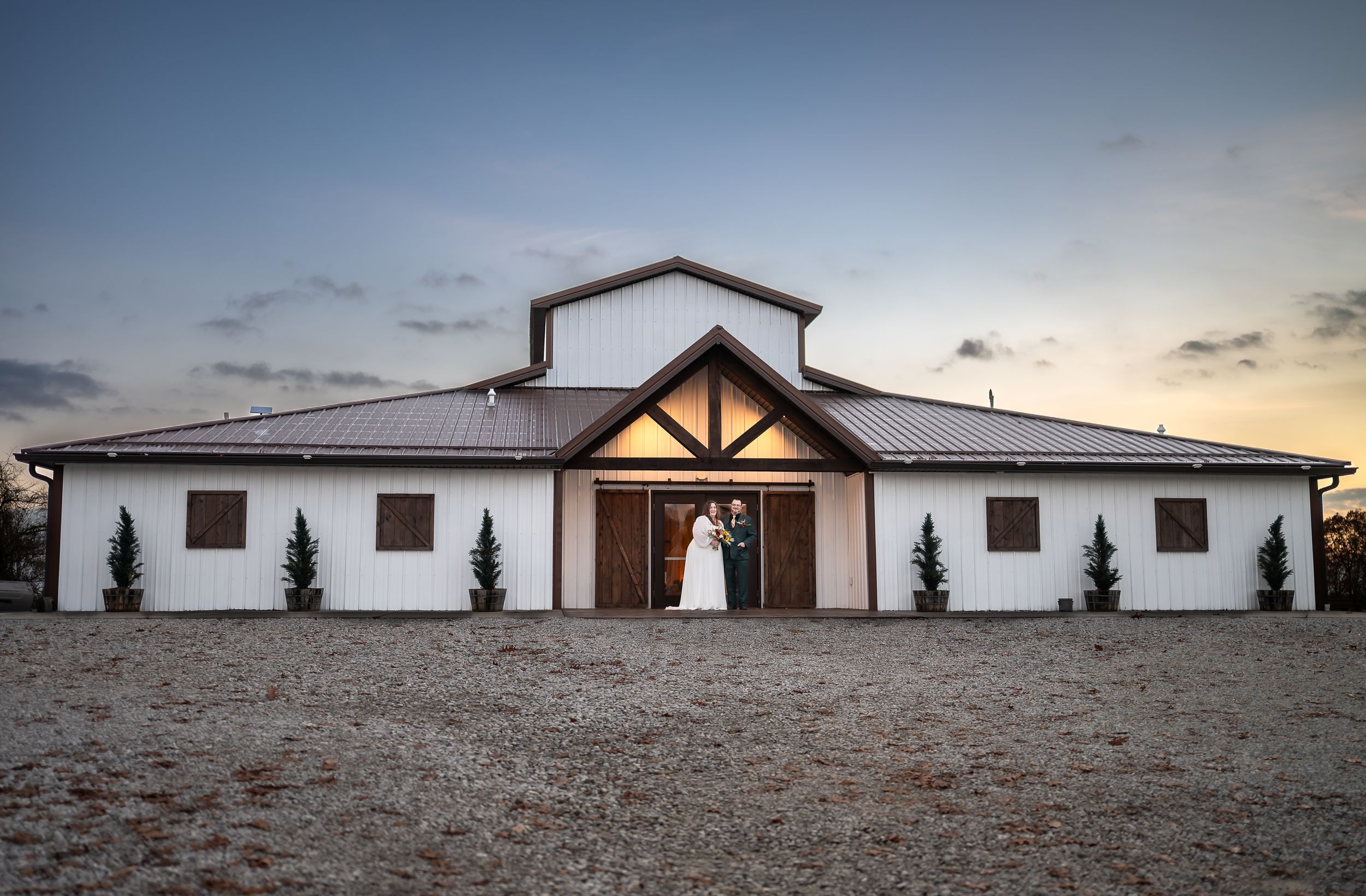 Panoramic view of a white ranch-style church building with wooden beams against a dramatic sunset sky in the desert.