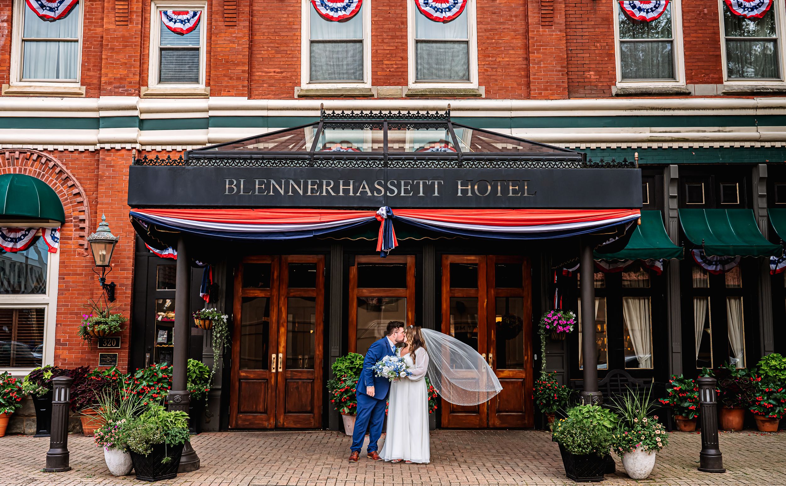 A brick exterior of storefronts lined with red, white, and blue bunting banners on an historic downtown building.
