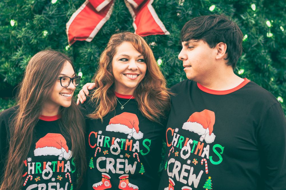 Three people wearing matching black Christmas Crew sweaters with Santa hats smile together outdoors during the holidays.