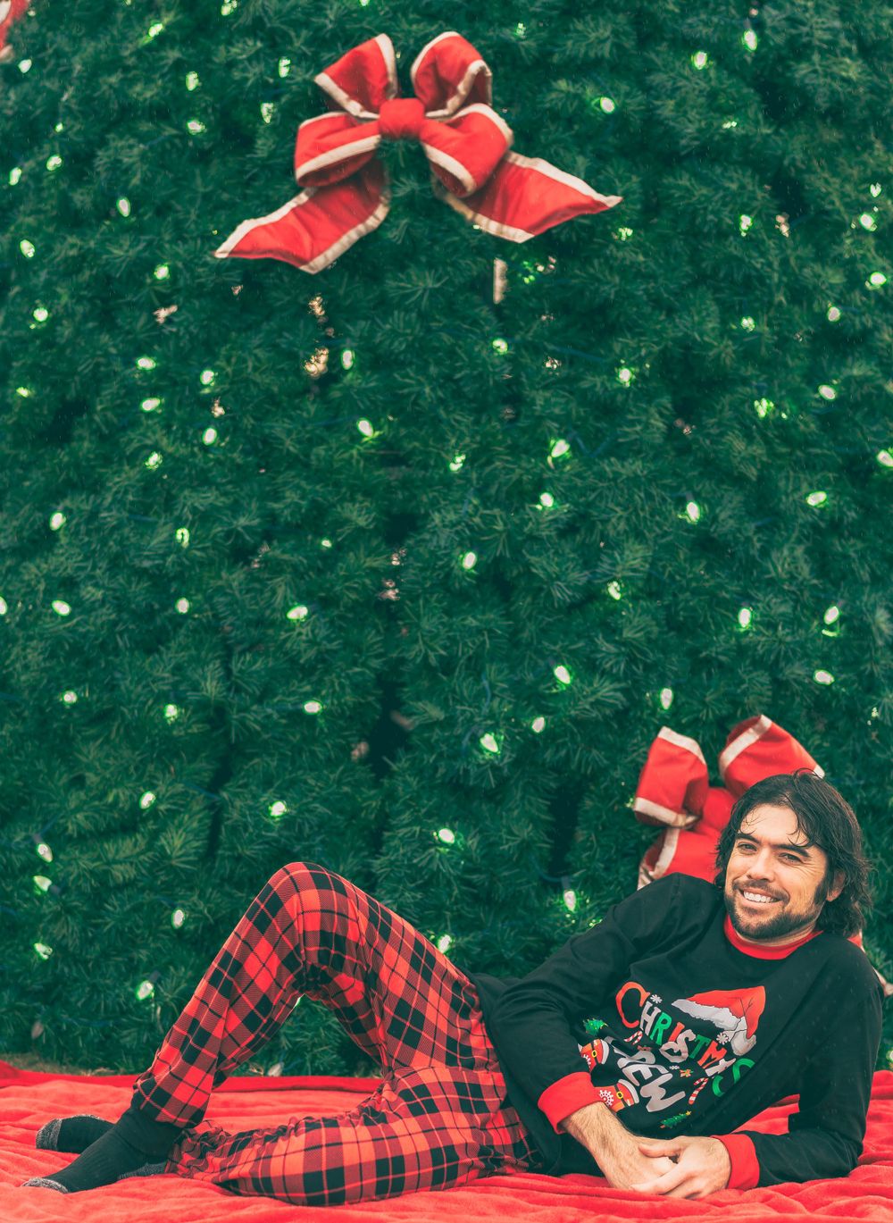 A festive holiday scene with plaid pajamas against a decorated green Christmas tree with red bows.