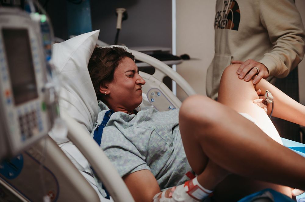 A patient grimaces in pain while laying in a hospital bed during labor and delivery.