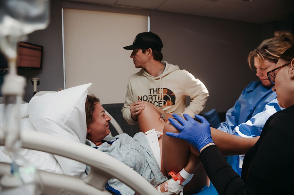 Medical staff and visitors gather around a patient lying in a hospital bed during a care session.