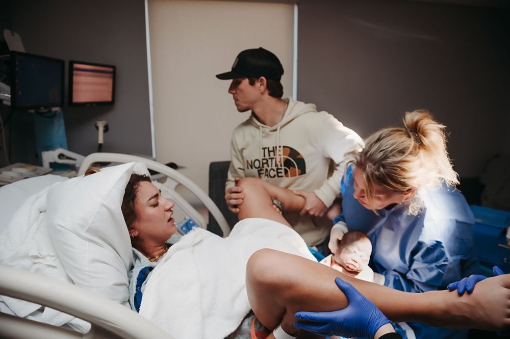 Healthcare providers assist a patient on a hospital bed during a birth.