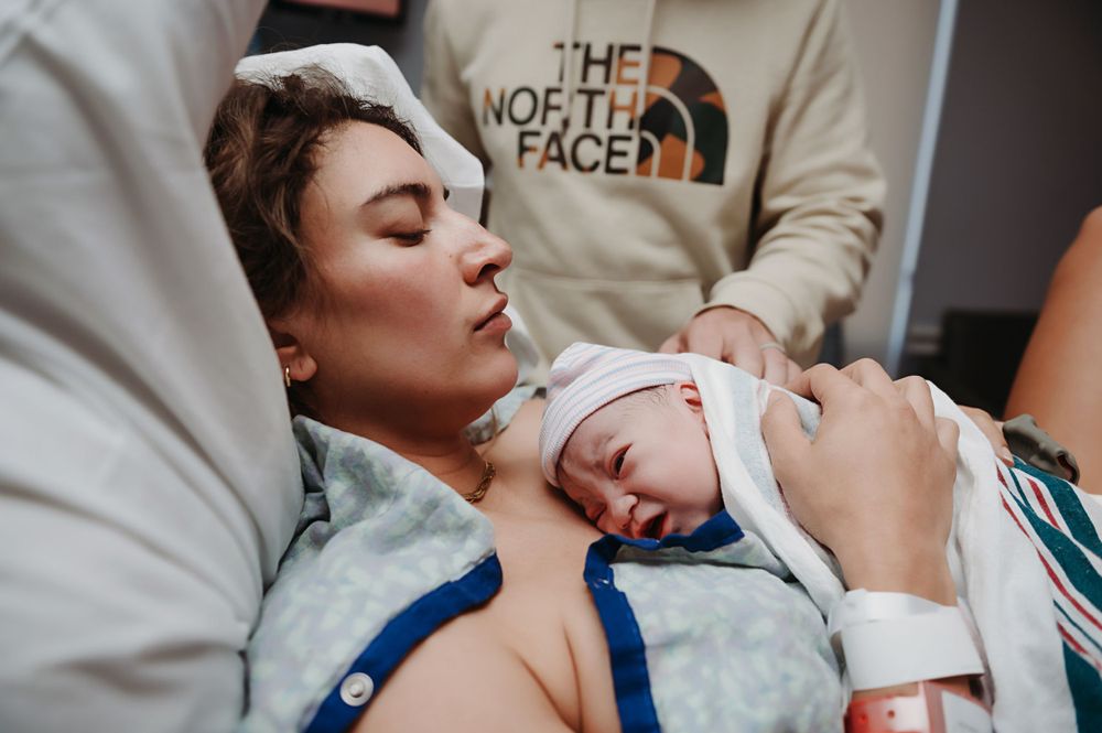 A newborn baby sleeps peacefully on a parent's chest during skin-to-skin contact while wearing a white hospital band.