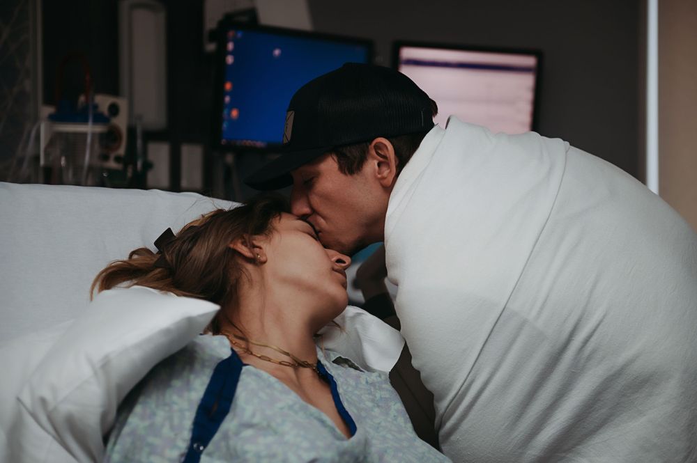 A tender moment between a couple in a hospital room with white bedding and soft lighting.