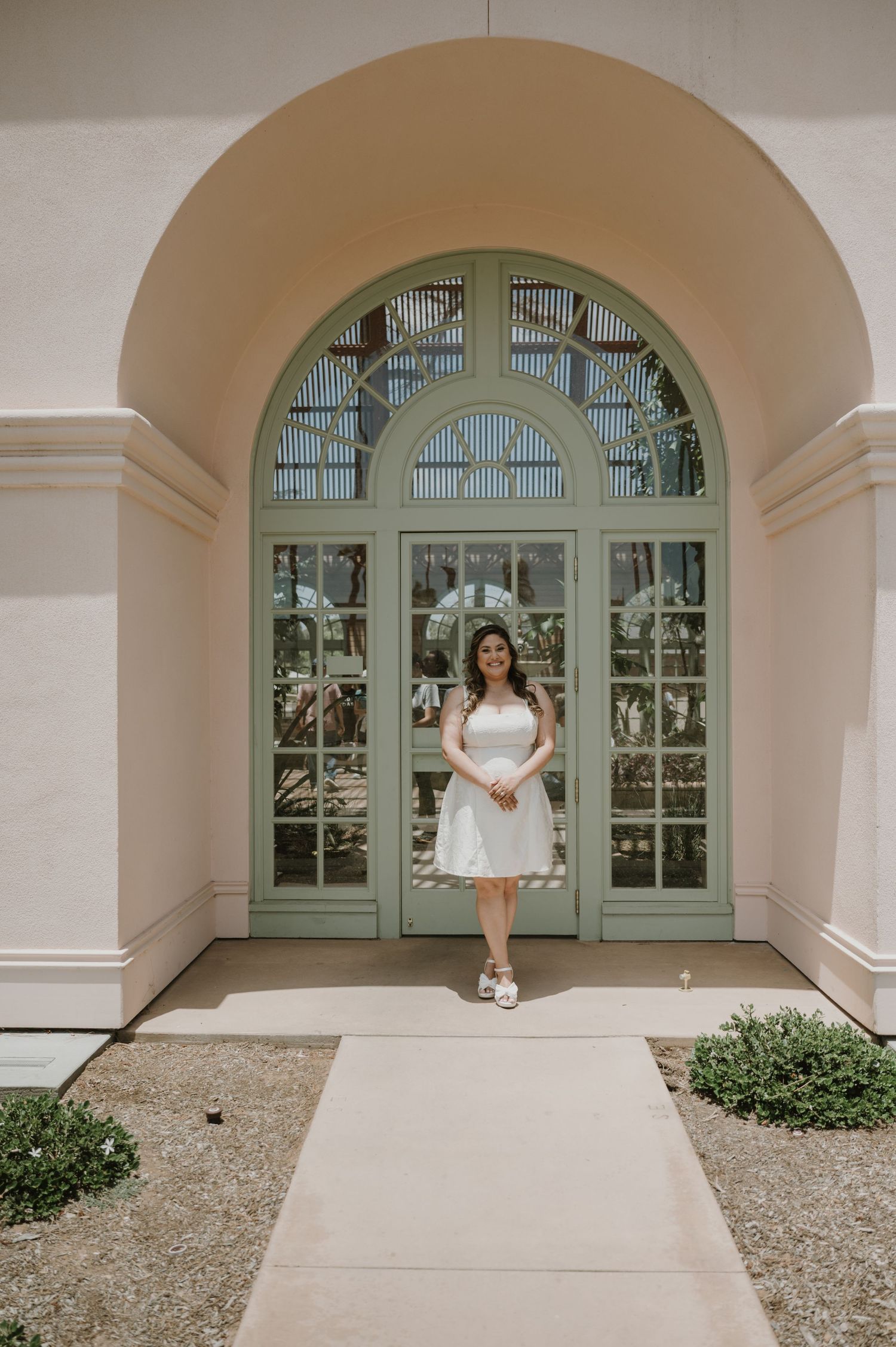 Woman in white dress poses under arched doorway with mint green window frame.