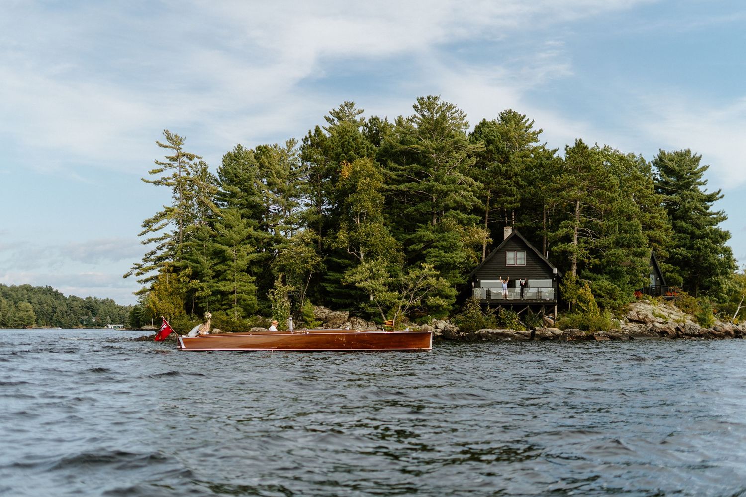 A scenic panoramic view of a lake with small forested islands and rocky shoreline under a bright blue summer sky.
