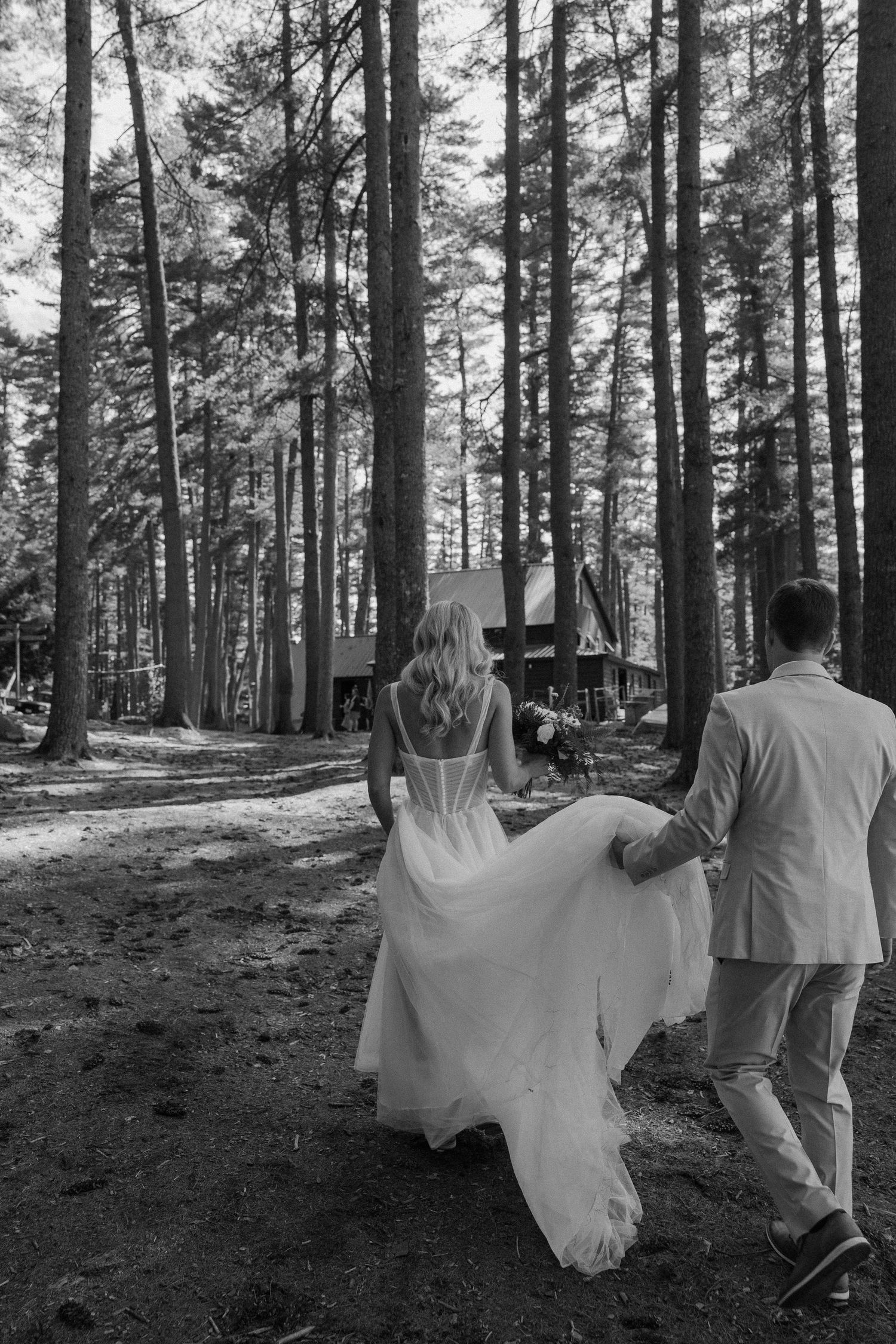 Black and white photo of couple walking through a pine forest.
