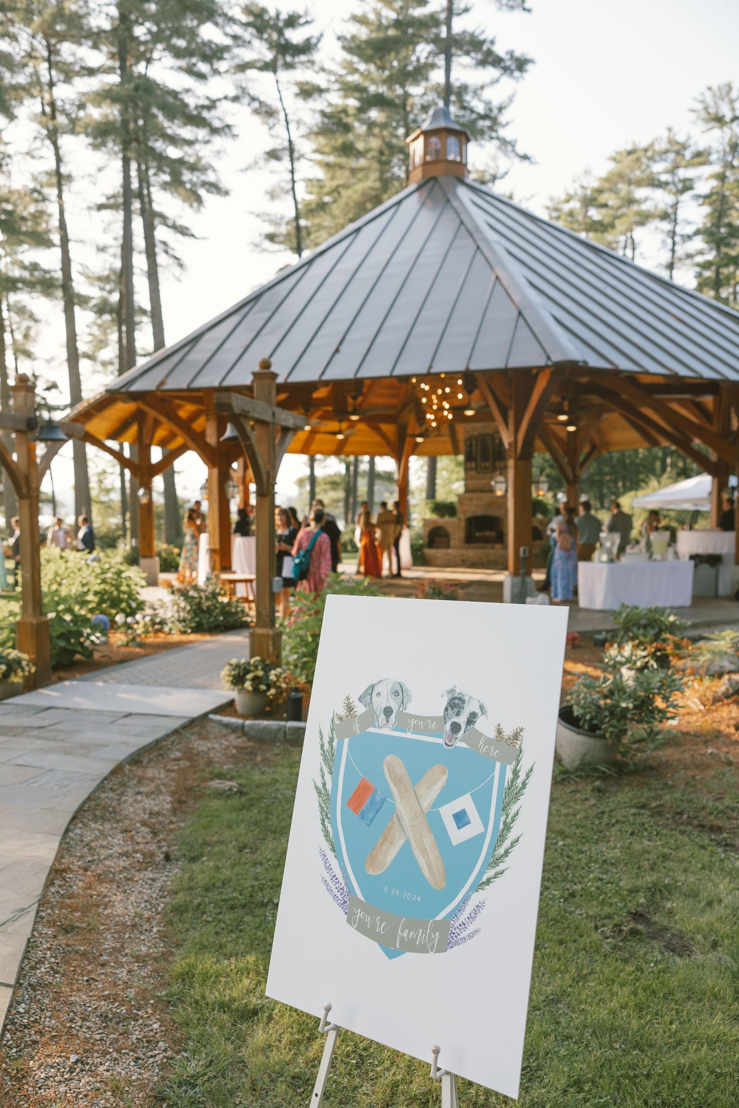 Outdoor wedding venue with covered gazebos and decorative signage among pine trees.