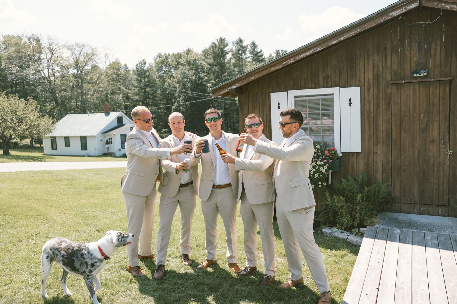 Wedding party in light colored attire posing outside a rustic wooden building.