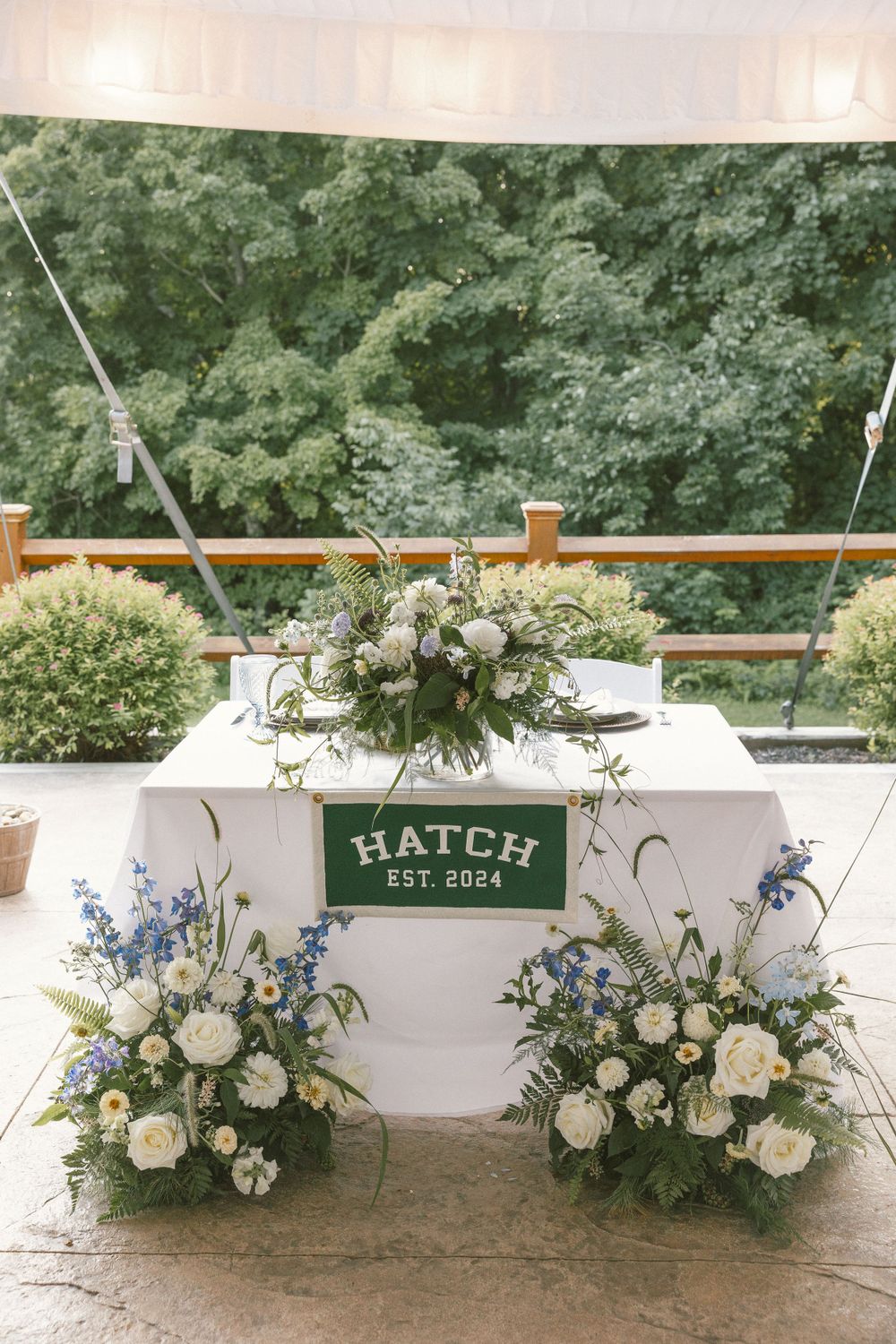 Elegant floral arrangements with white and blue flowers decorate a white bar with 'Hatch' signage.