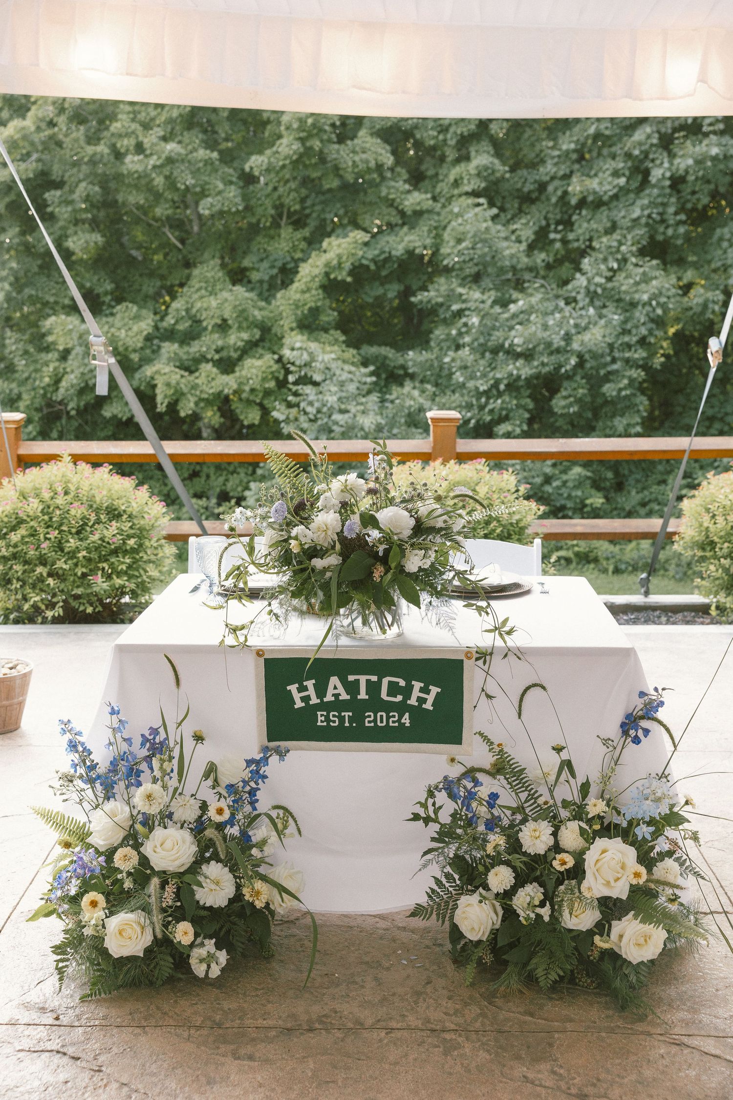 Elegant floral arrangements with white and blue flowers decorate a white bar with 'Hatch' signage.