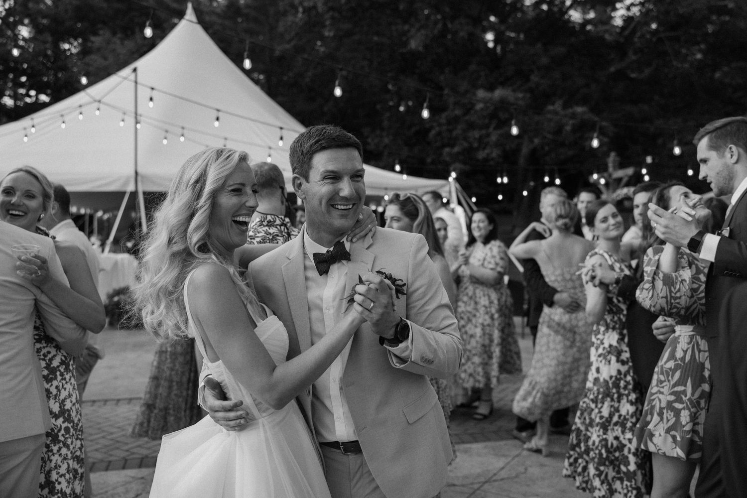 Wedding guests dance and celebrate at an outdoor evening reception.