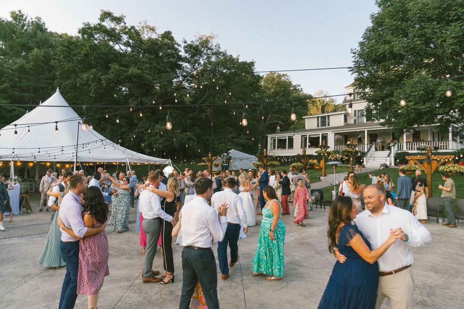 Couples dancing together at an outdoor summer celebration under string lights.