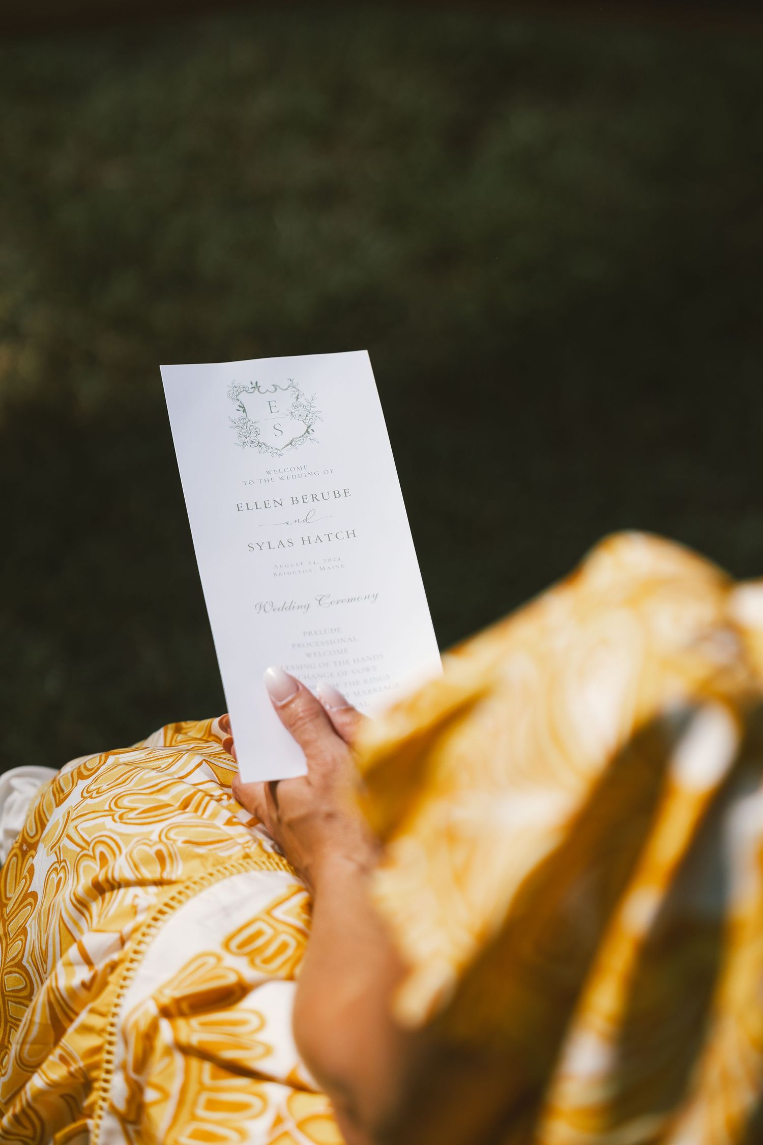 A wedding invitation or card being held up against a blurred golden fabric background.