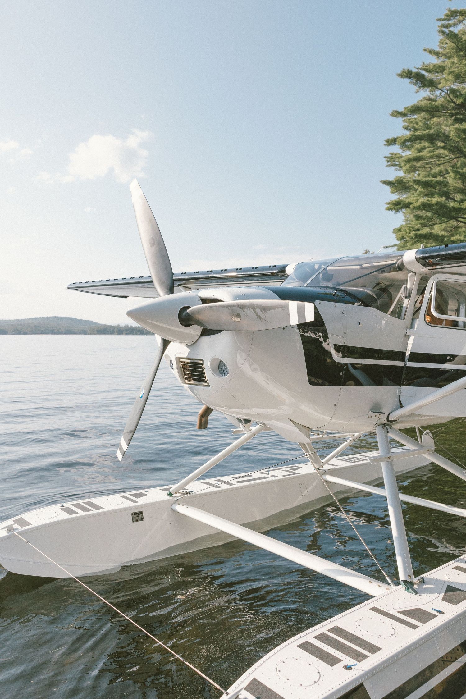 White seaplane with floats docked on calm lake with mountains in background.
