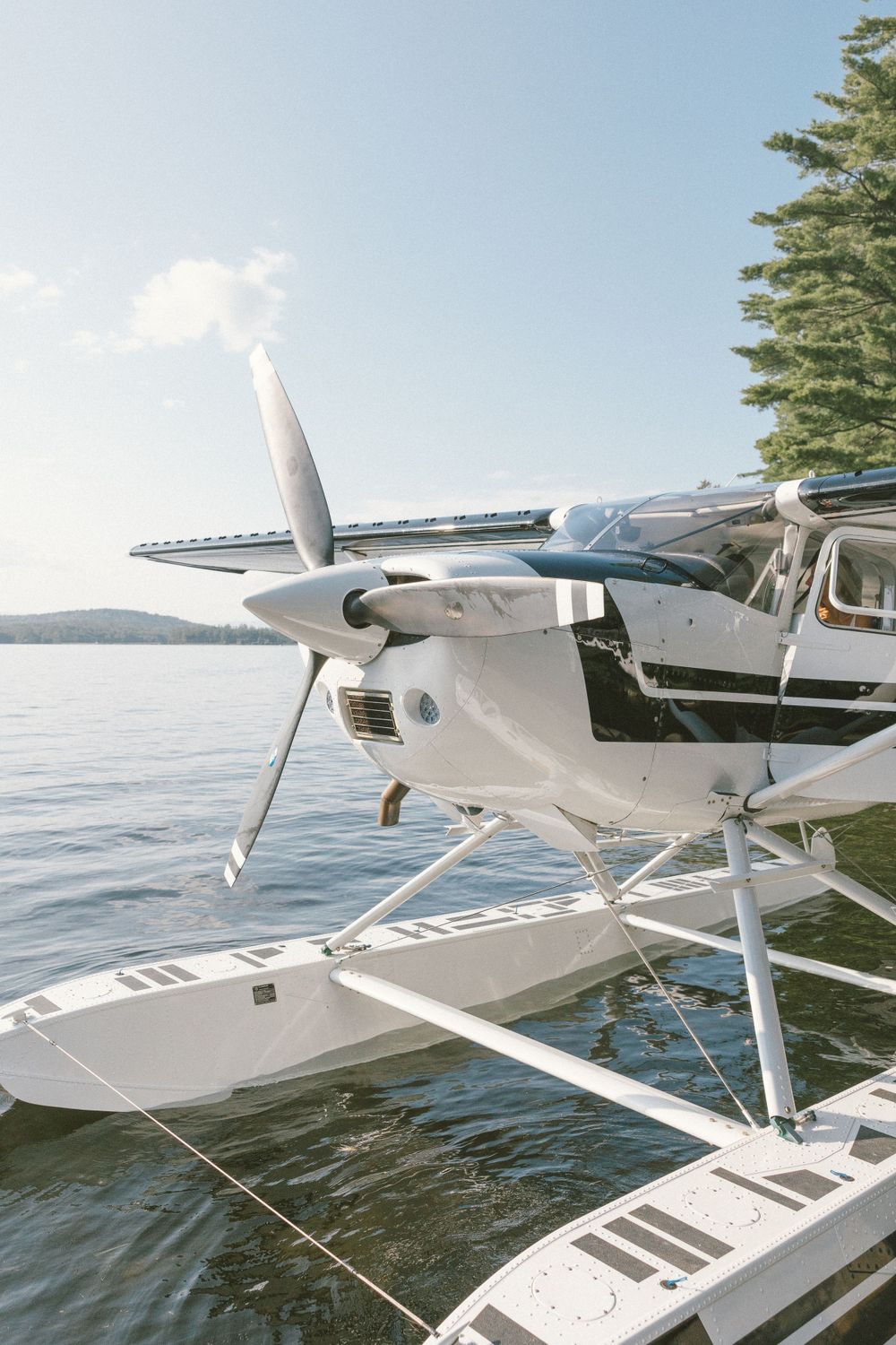 White seaplane with floats docked on calm lake with mountains in background.