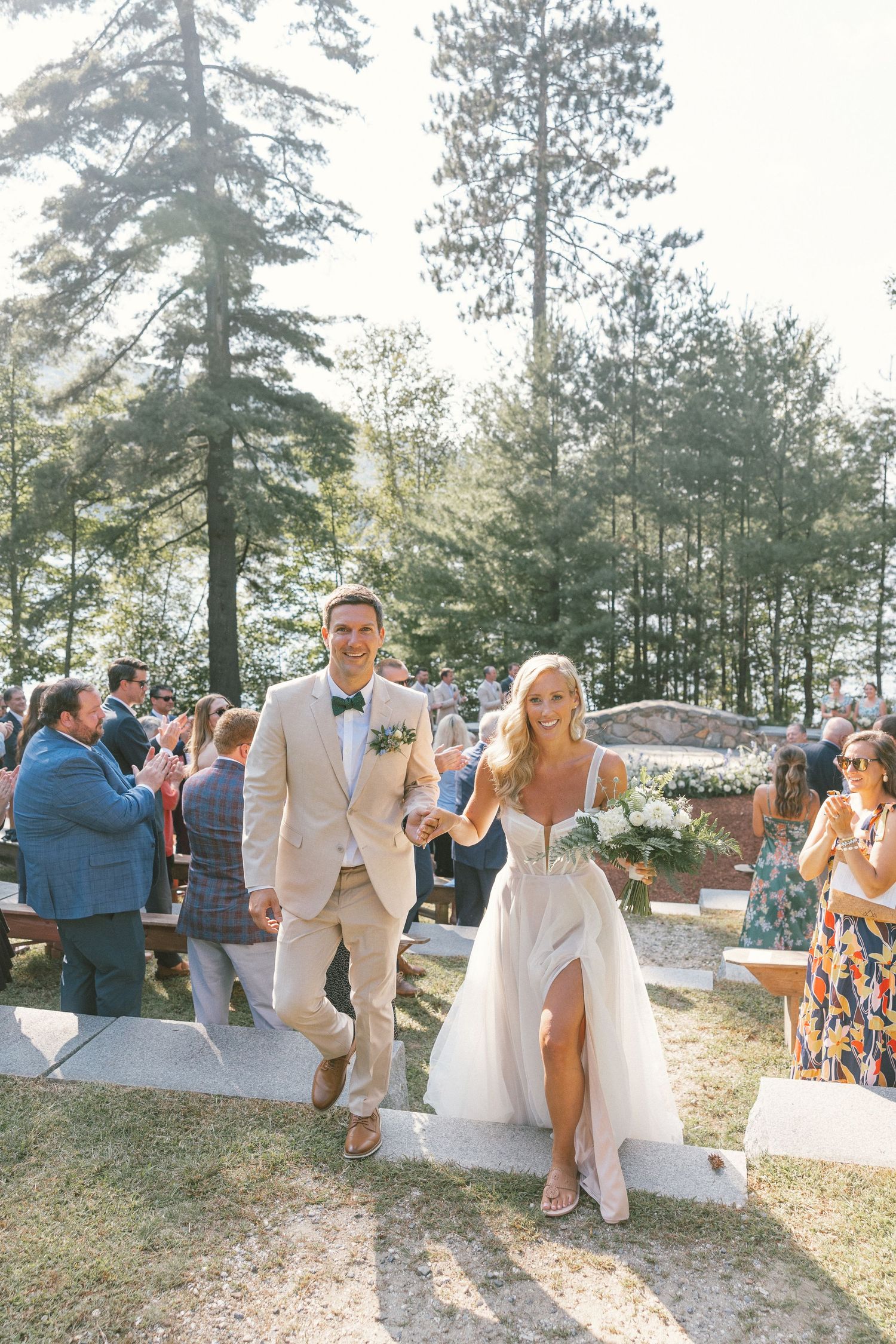 Wedding celebration in a sunny outdoor pine forest setting with guests in summer attire.