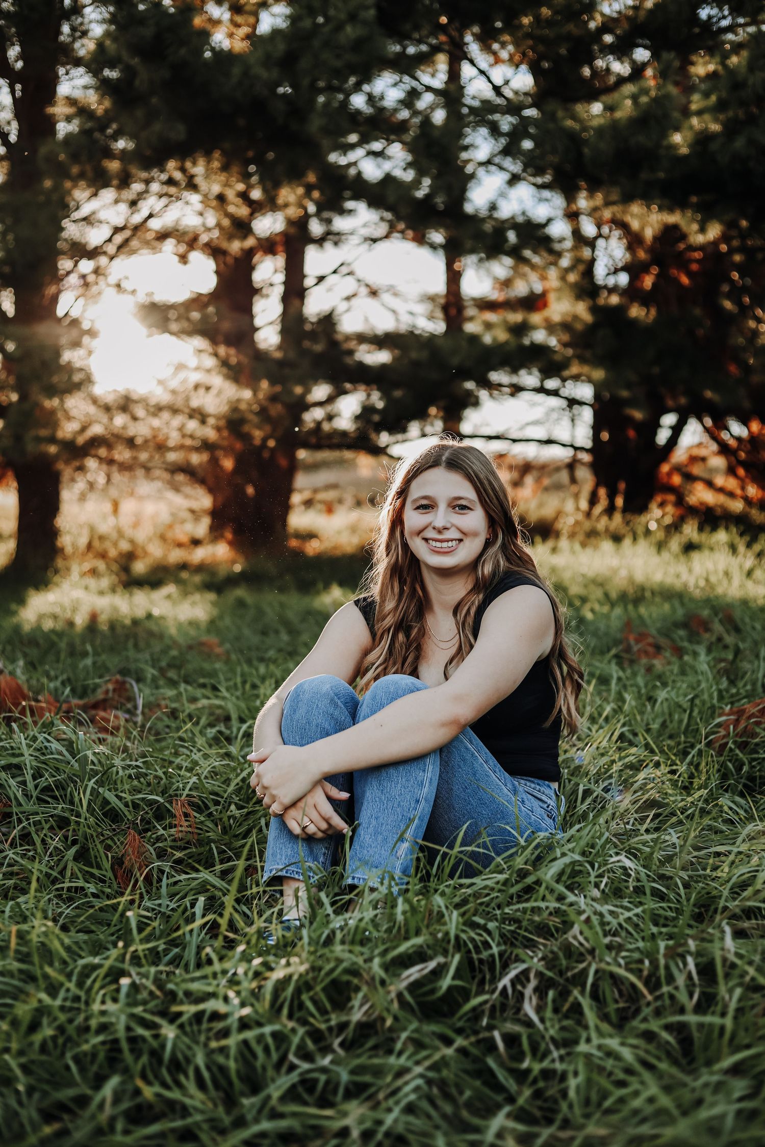 Casual outdoor portrait session in tall grass with sunset lighting through trees. Senior photography