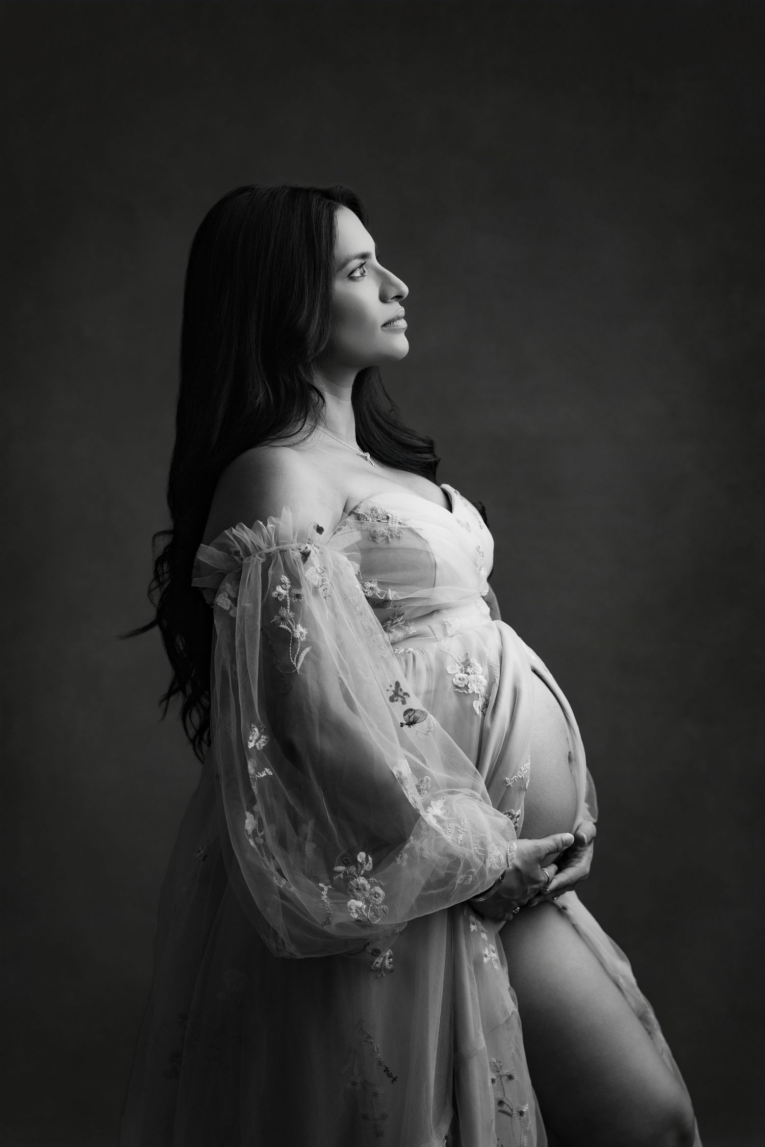 A black and white artistic maternity photoshoot series showing a pregnant figure in a flowing white dress.