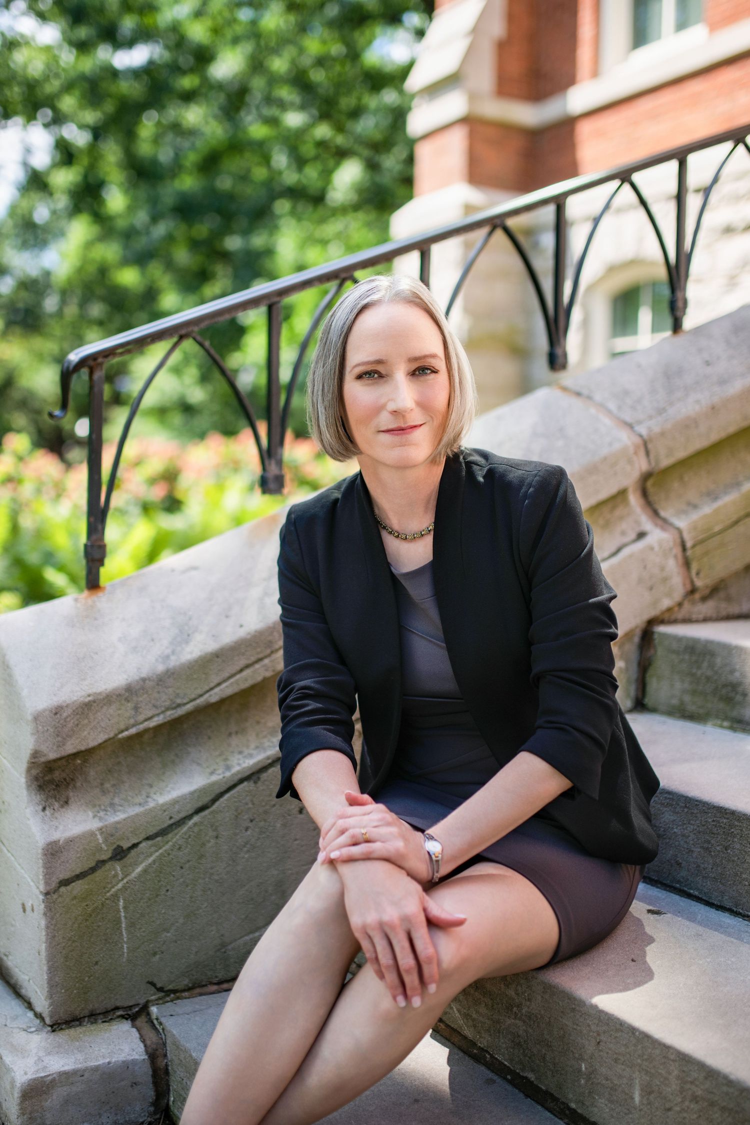 Professional portrait outdoors on a college campus with a bright smile and suit jacket casually draped over shoulder.