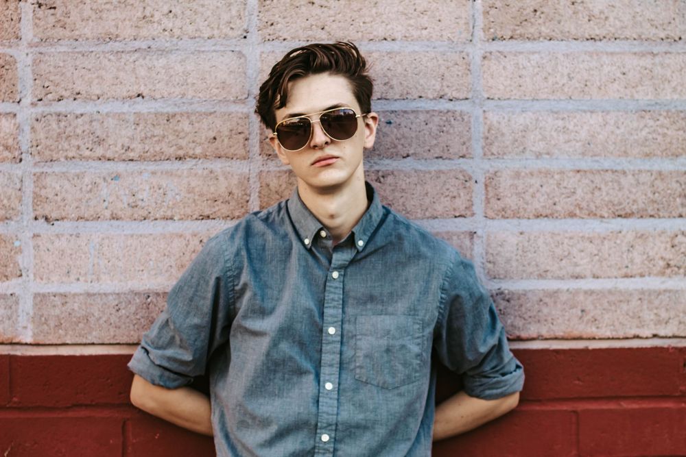 Man leans against brick wall for moody solo portraits.